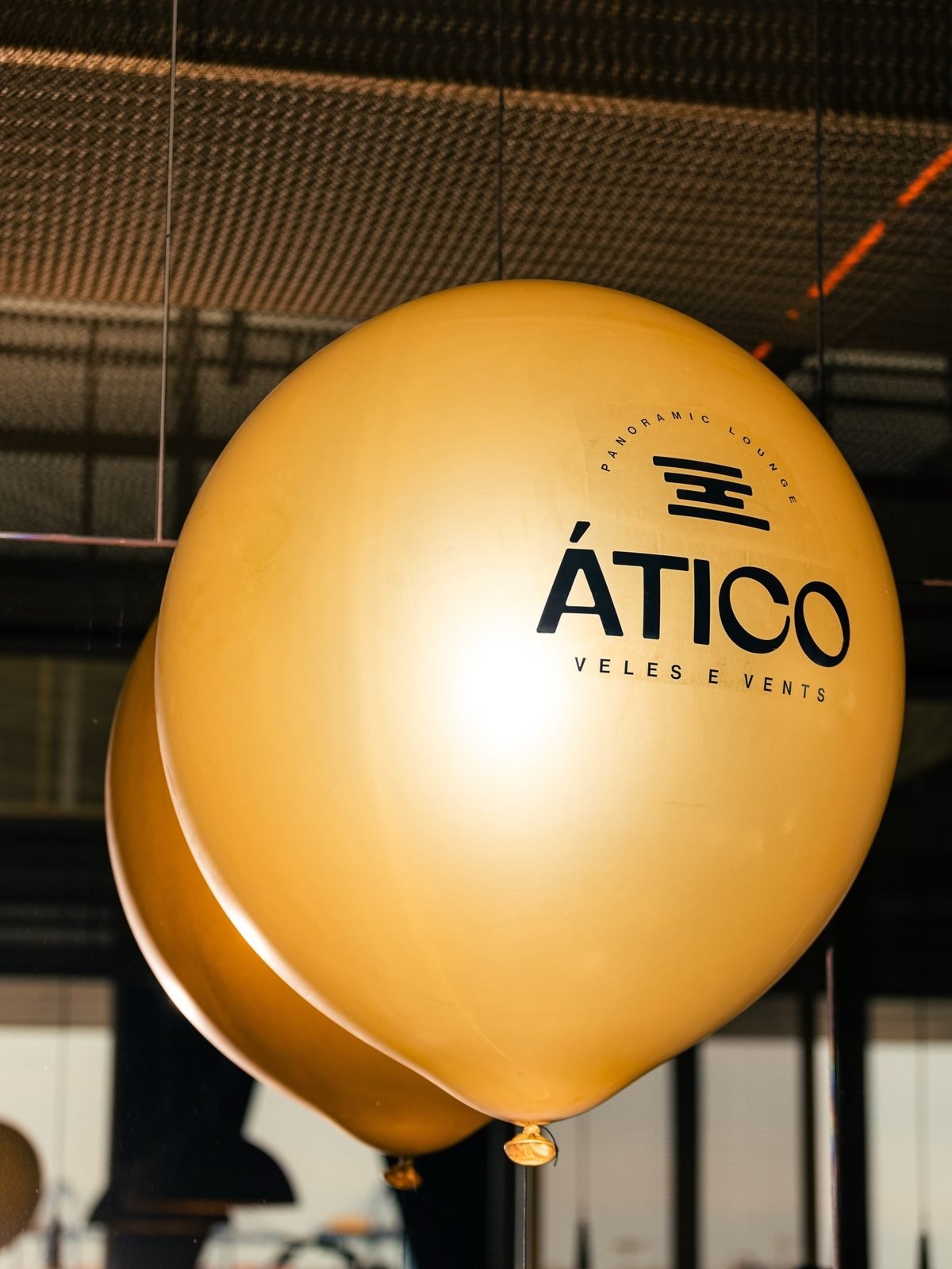 Globos dorados con el logotipo ÁTICO impreso en negro, suspendidos del techo