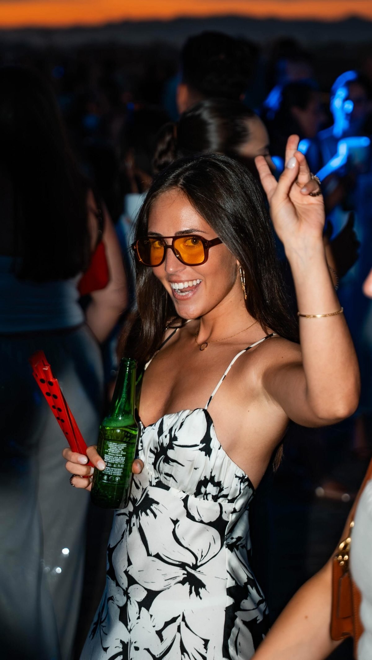 Asistente sonriendo con gafas naranjas durante una fiesta al atardecer en ÁTICO
