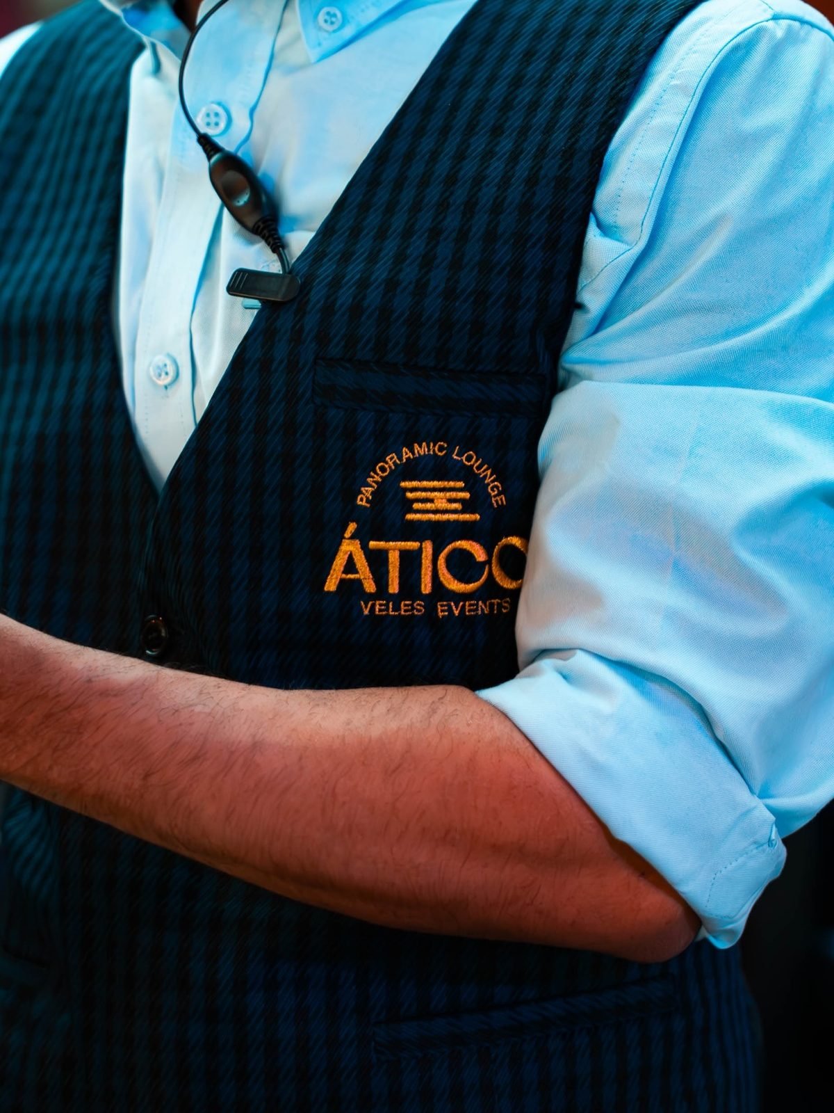 Uniforme del personal: chaleco azul marino con bordado del logotipo ÁTICO en hilo dorado