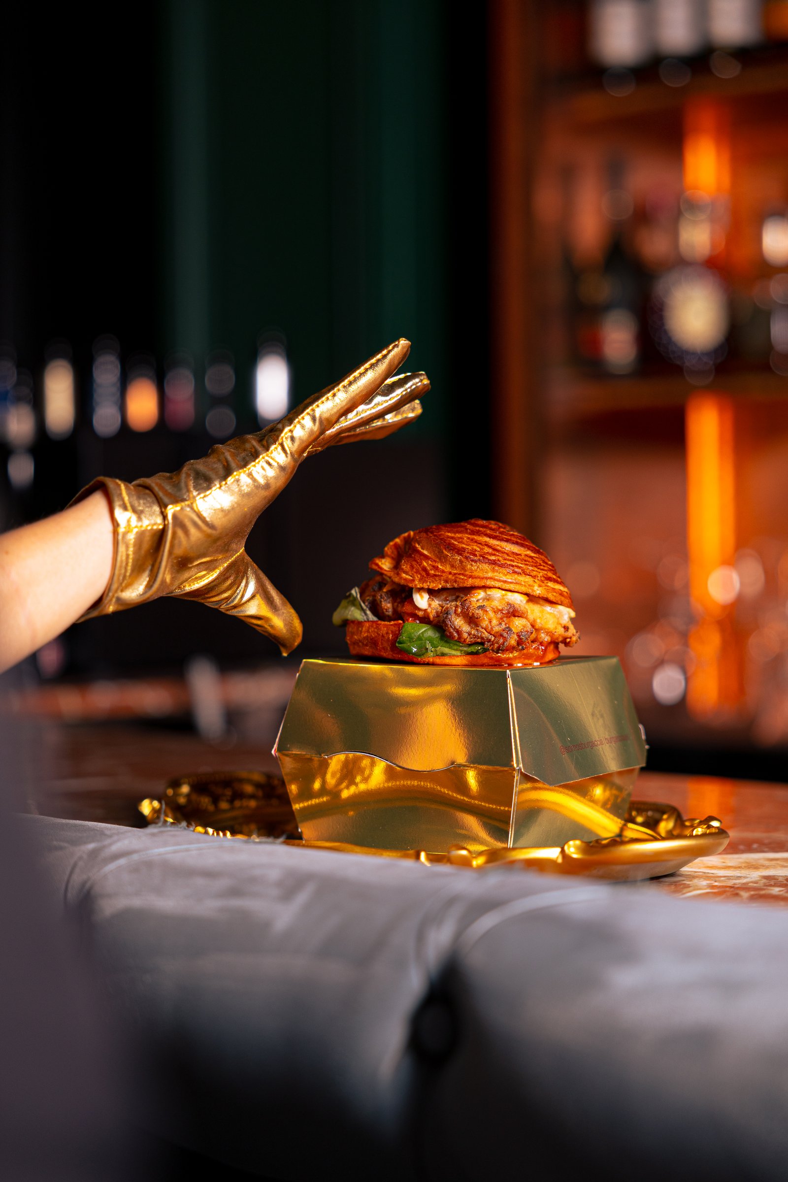 Bodegón de focaccia, hamburguesa y bebida con iluminación cálida tipo restaurante de mantel