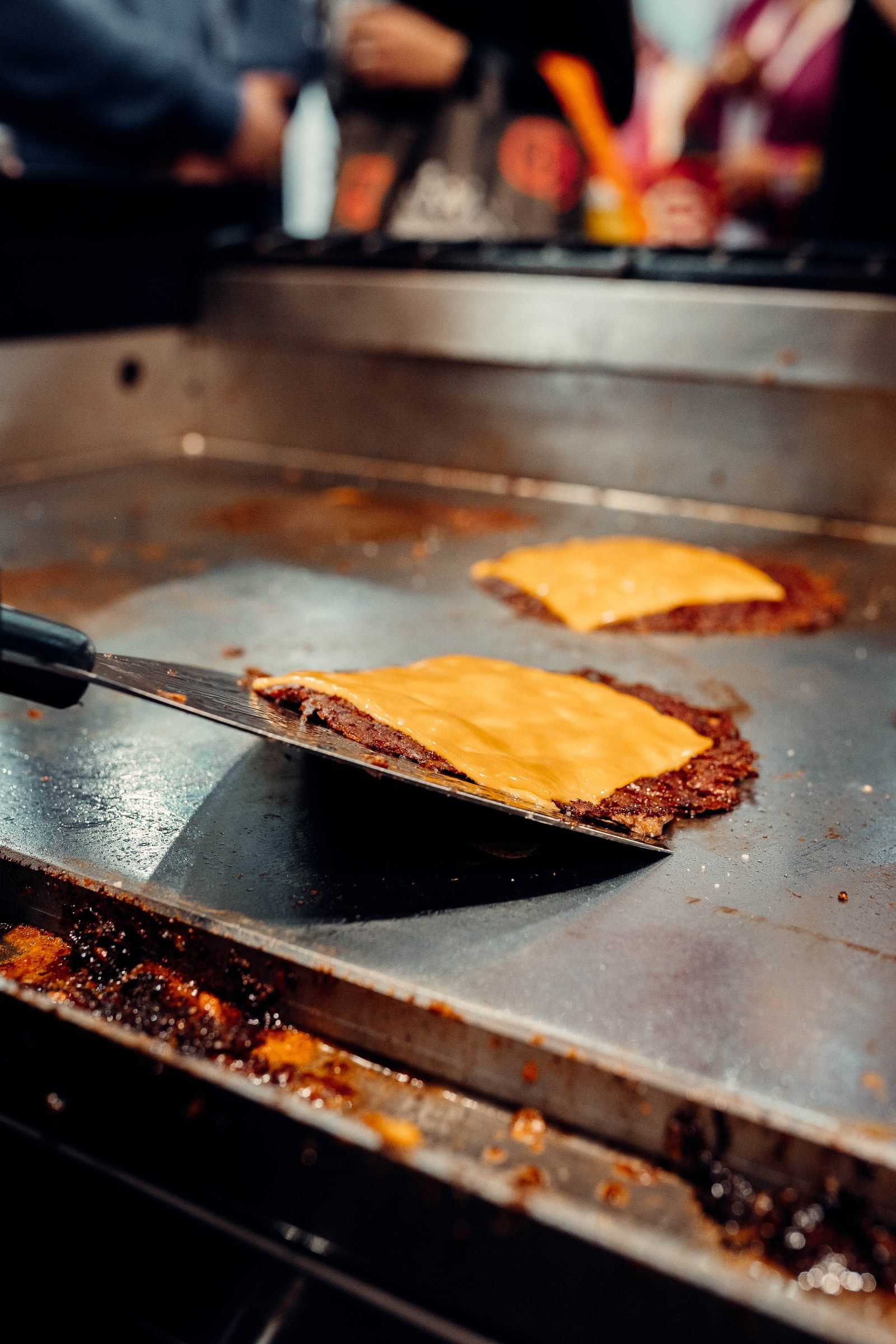 Espátula levantando una smash burger con cheddar fundido directamente desde la plancha caliente — CRUASH