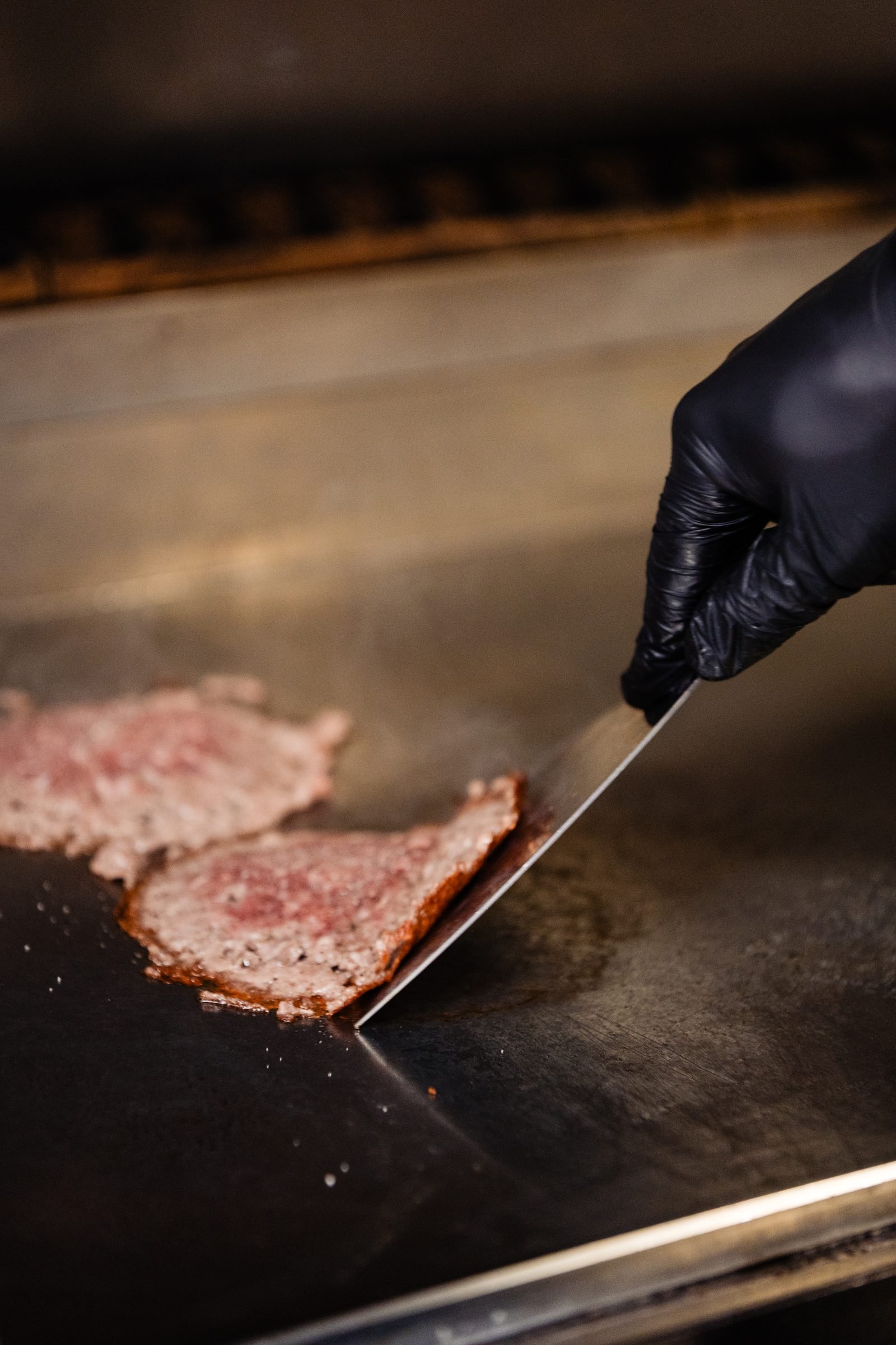 Smasher de acero CRUASH en acción aplastando carne sobre plancha caliente — fotografía de producto en uso