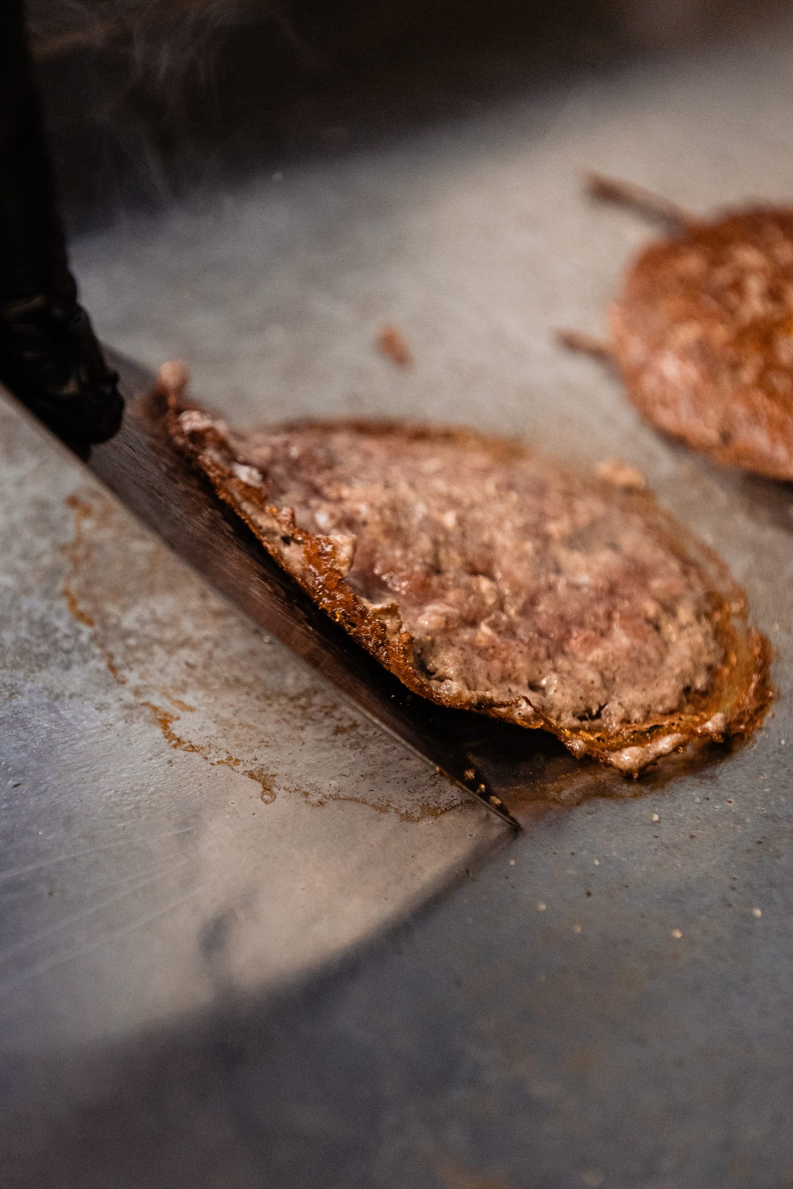 Smashburger con corteza crujiente recién levantada de la plancha con espátula — primer plano CRUASH