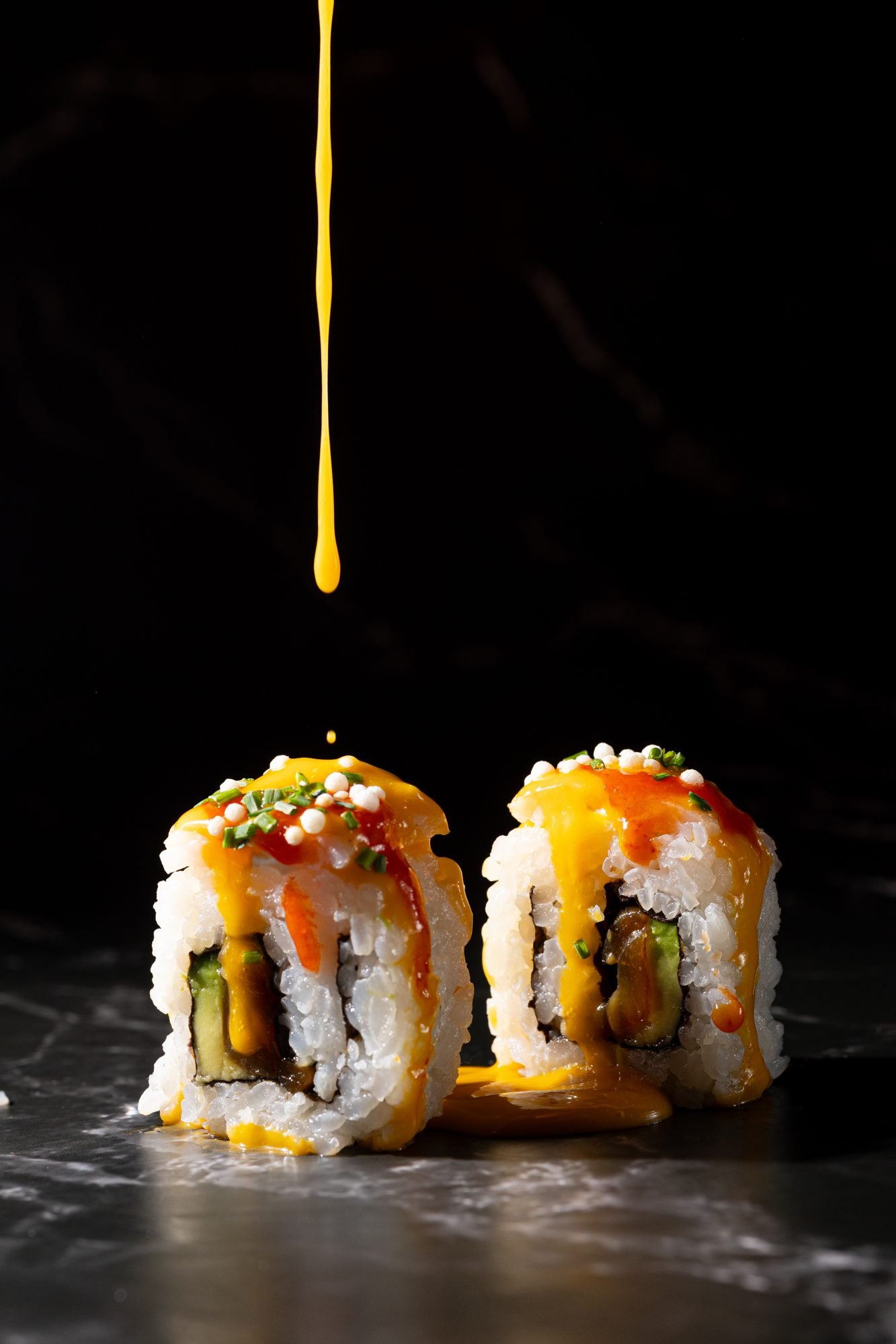 Uramaki JAPOMEX bañado por chorro de salsa amarilla sobre fondo negro — fotografía gastronómica editorial