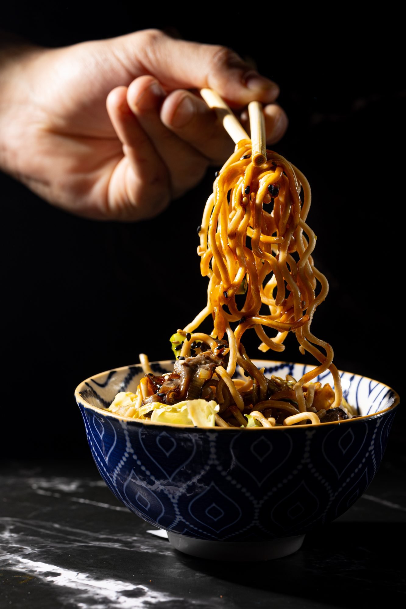 Cuenco de ramen con palillos levantando los fideos sobre cerámica japonesa azul cobalto — JAPOMEX