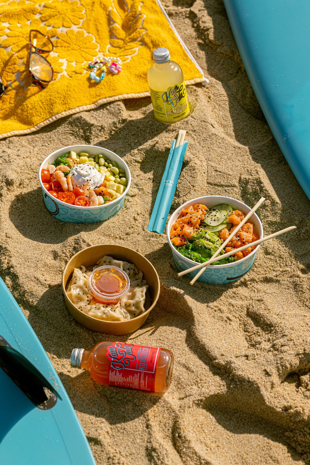 Picnic de Mahalo Poké sobre toalla amarilla en la arena de la playa