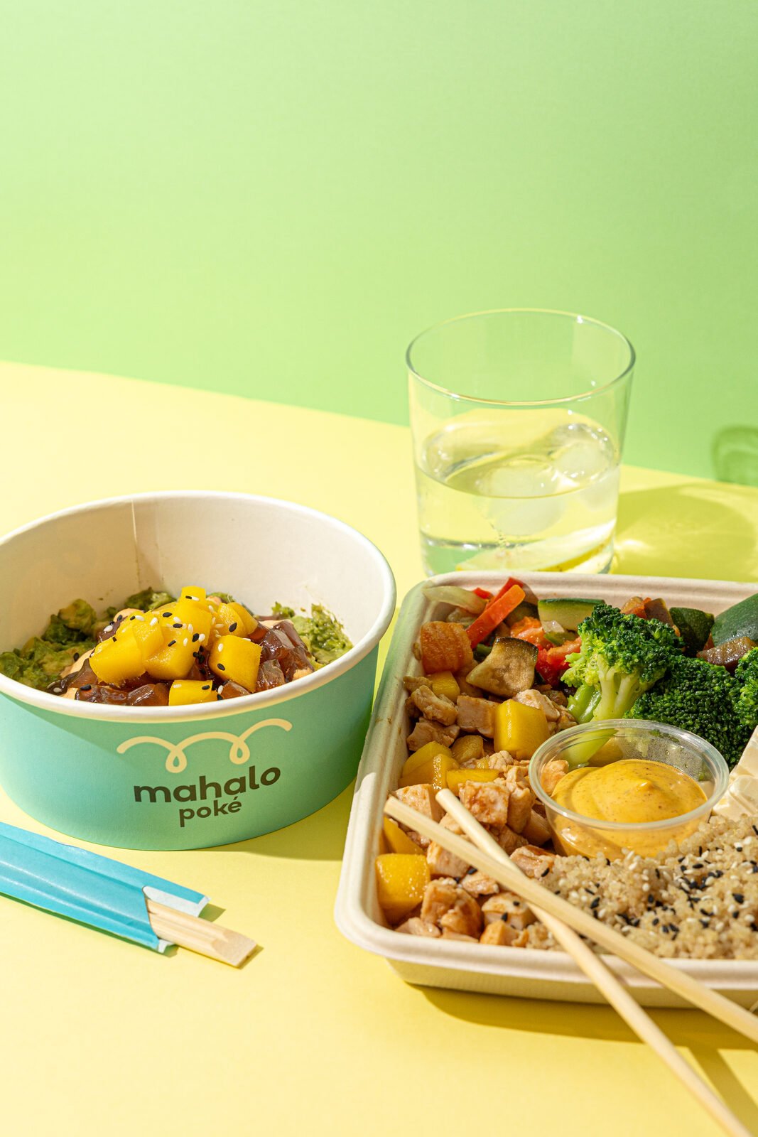 Bowl Mahalo branded junto a tray con verduras y pollo sobre superficie amarilla y verde
