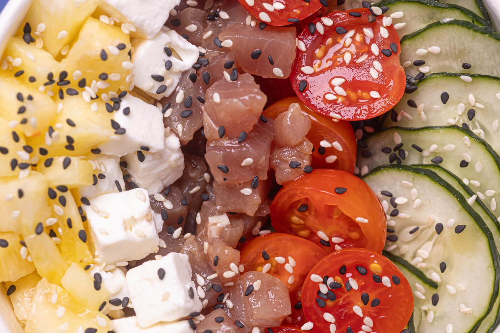 Detalle macro de bowl de poké — atún, feta, tomate cherry y pepino con sésamo blanco y negro