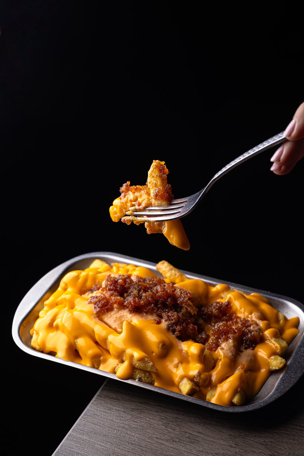 Tenedor levantando patatas fritas con queso fundido y bacon sobre tray metálico — Vibra Burger