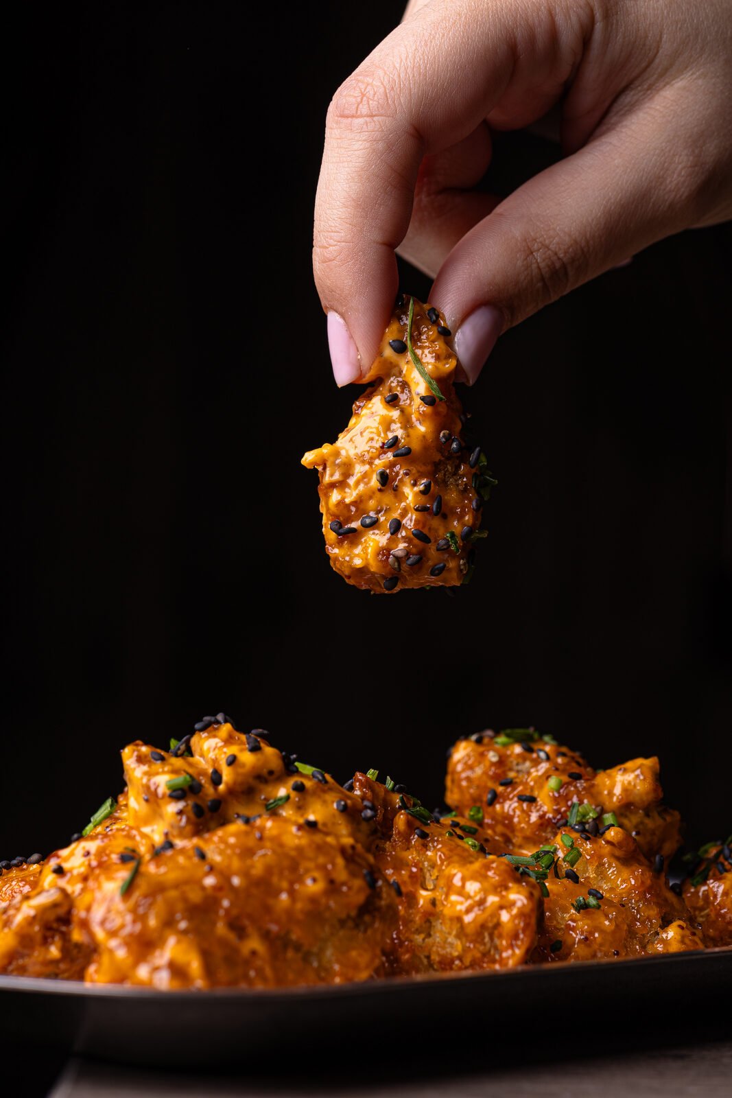 Mano cogiendo nuggets de pollo glaseados con sésamo y cebollino — Vibra Burger