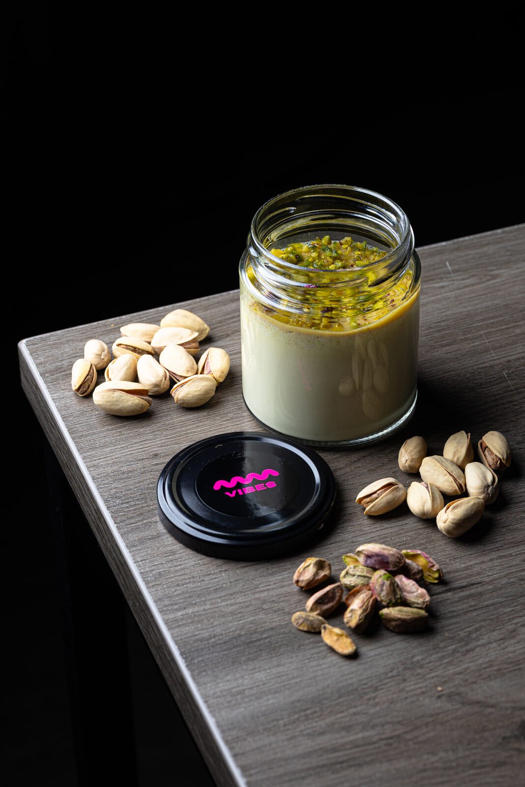 Tarro de salsa de pistacho VIBES con pistachos pelados y enteros sobre madera oscura