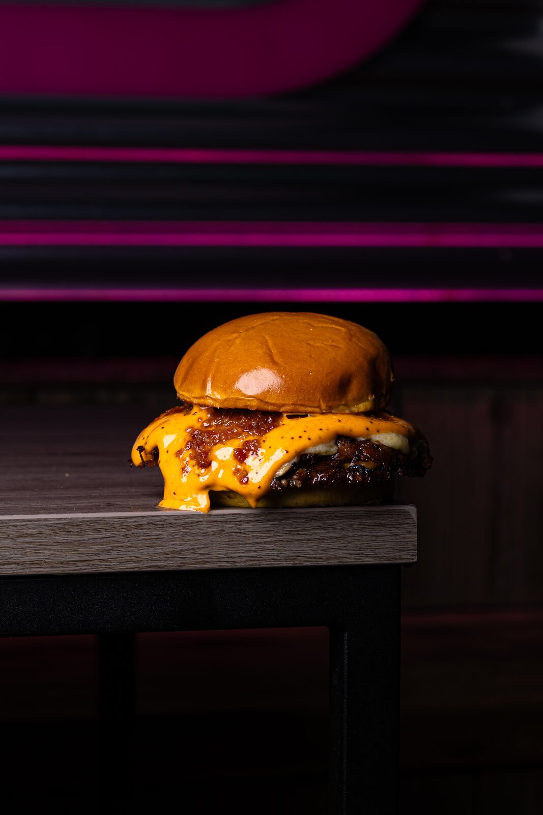 Smash burger con queso americano derretido sobre fondo magenta neón — Vibra Burger