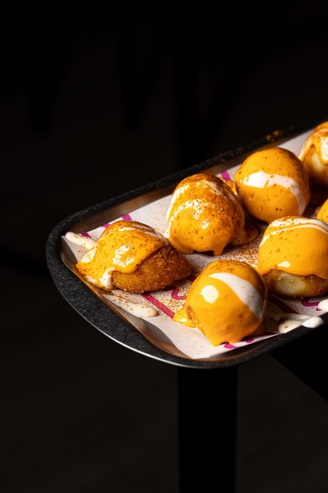 Bandeja de croquetas o bombones de queso bañados en salsa cheddar y rosa picante