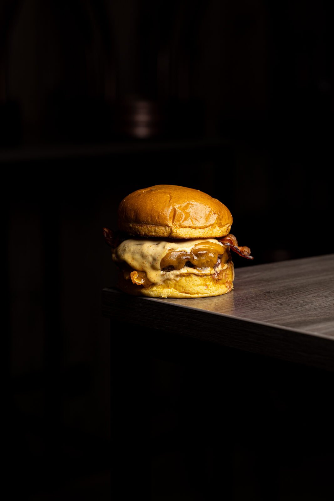 Smash burger con bacon iluminada en spotlight cinematográfico sobre fondo negro