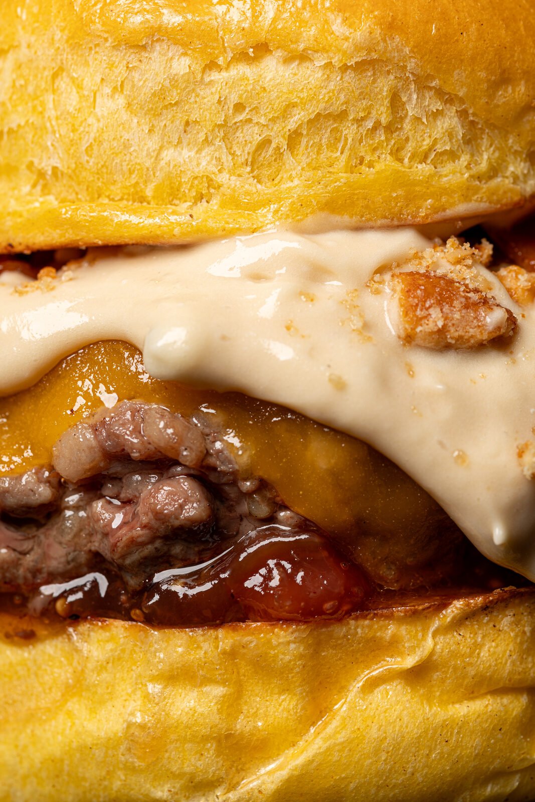 Macro extremo de smash burger con salsa cremosa cayendo sobre el queso fundido y carne sellada